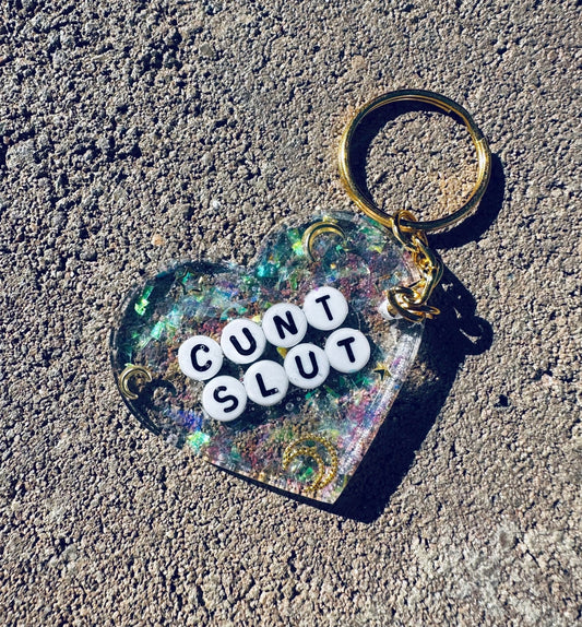 Funny Glitter heart keychain with 'CUNT SLUT' text, gold keyring and attached dark charm