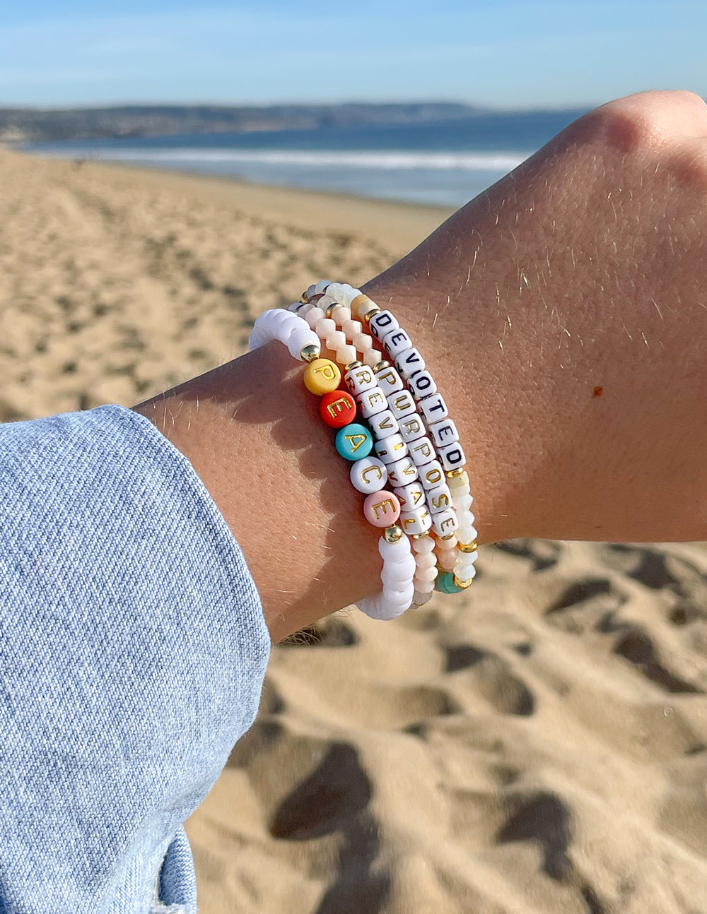 Elevated Faith Christian Jewelry Bracelet with colorful letter beads displayed on a sandy beach