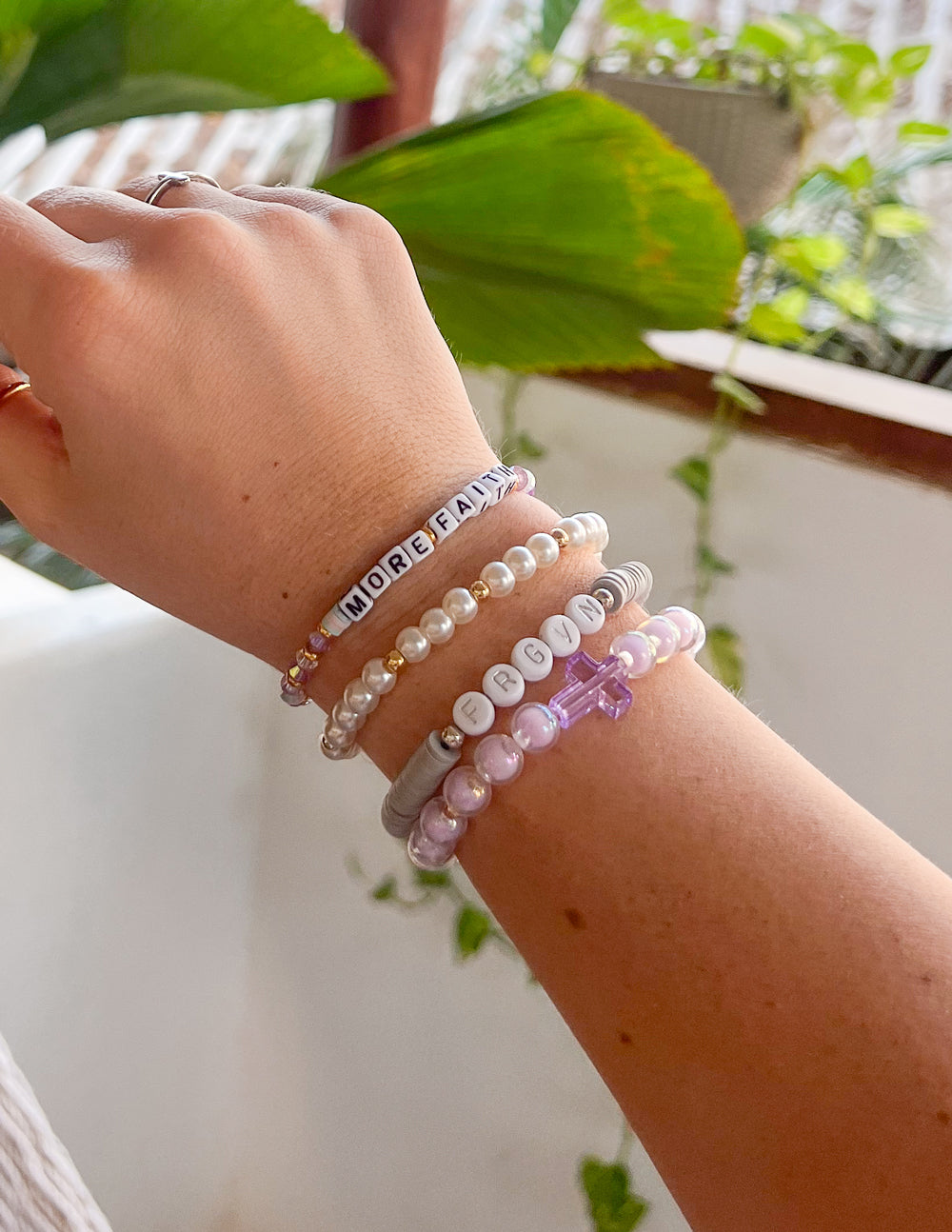 Letter Bracelet from Elevated Faith, part of a stack featuring Christian Jewelry Bracelet in purple and white beads