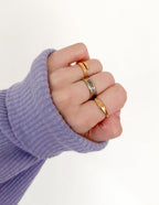 Three Elevated Faith rings featuring Christian Jewelry in gold and silver on a hand wearing a purple sleeve