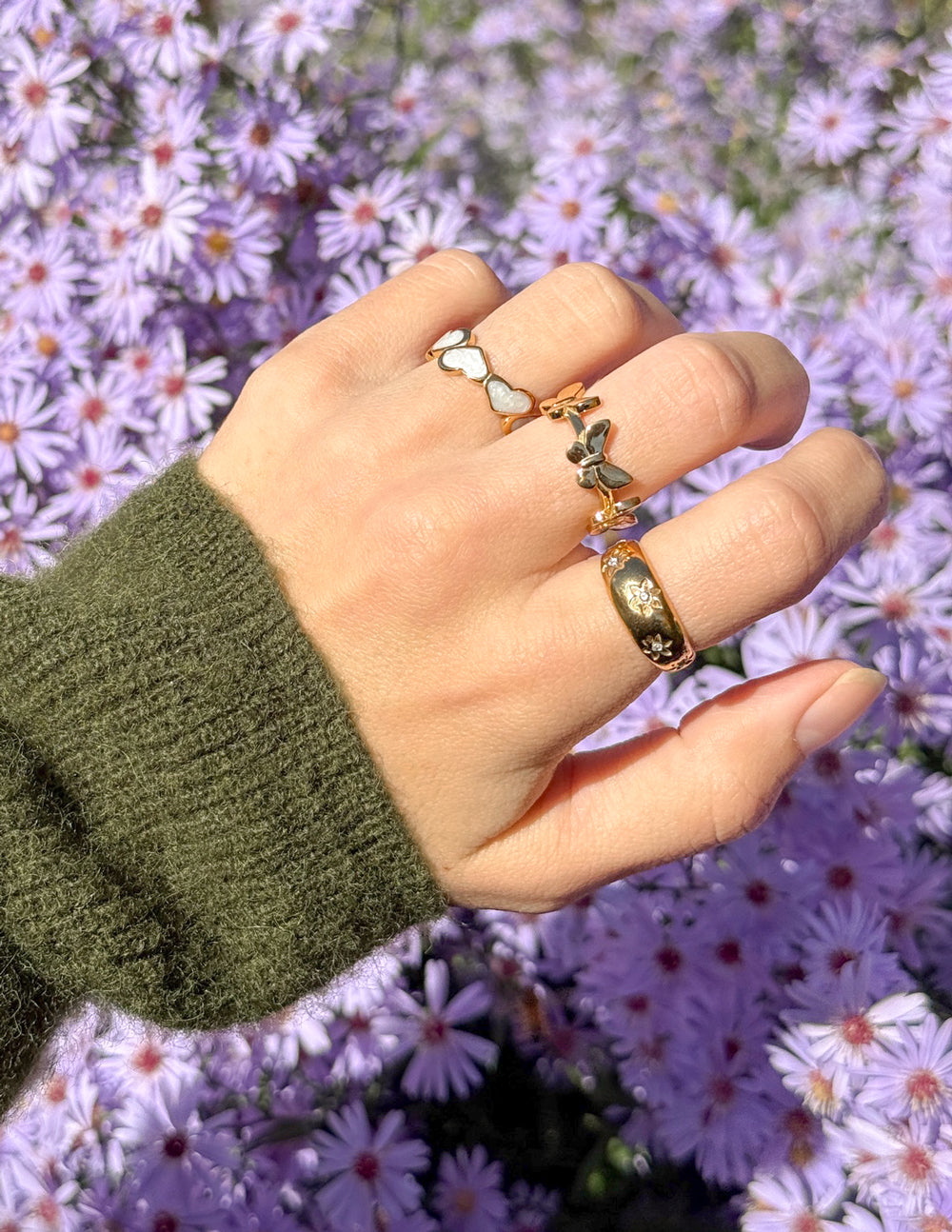 Elevated Faith Christian Jewelry featuring three stylish rings on a hand among purple flowers
