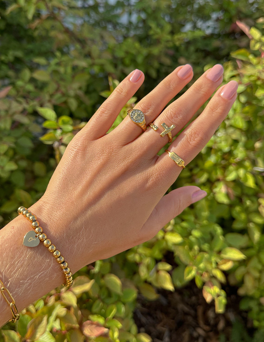 Elevated Faith Christian Jewelry collection featuring rings and a bracelet on a hand against greenery