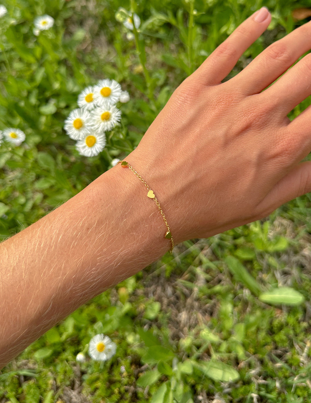 Elevated Faith Christian Jewelry Bracelet in gold with delicate heart accents on a hand among flowers