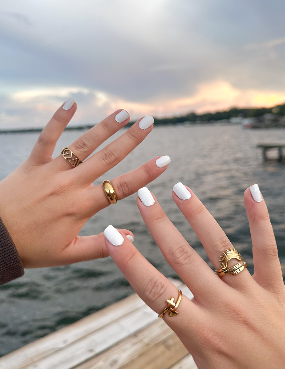 Two hands displaying different Elevated Faith rings as stylish Christian Jewelry against a scenic waterfront