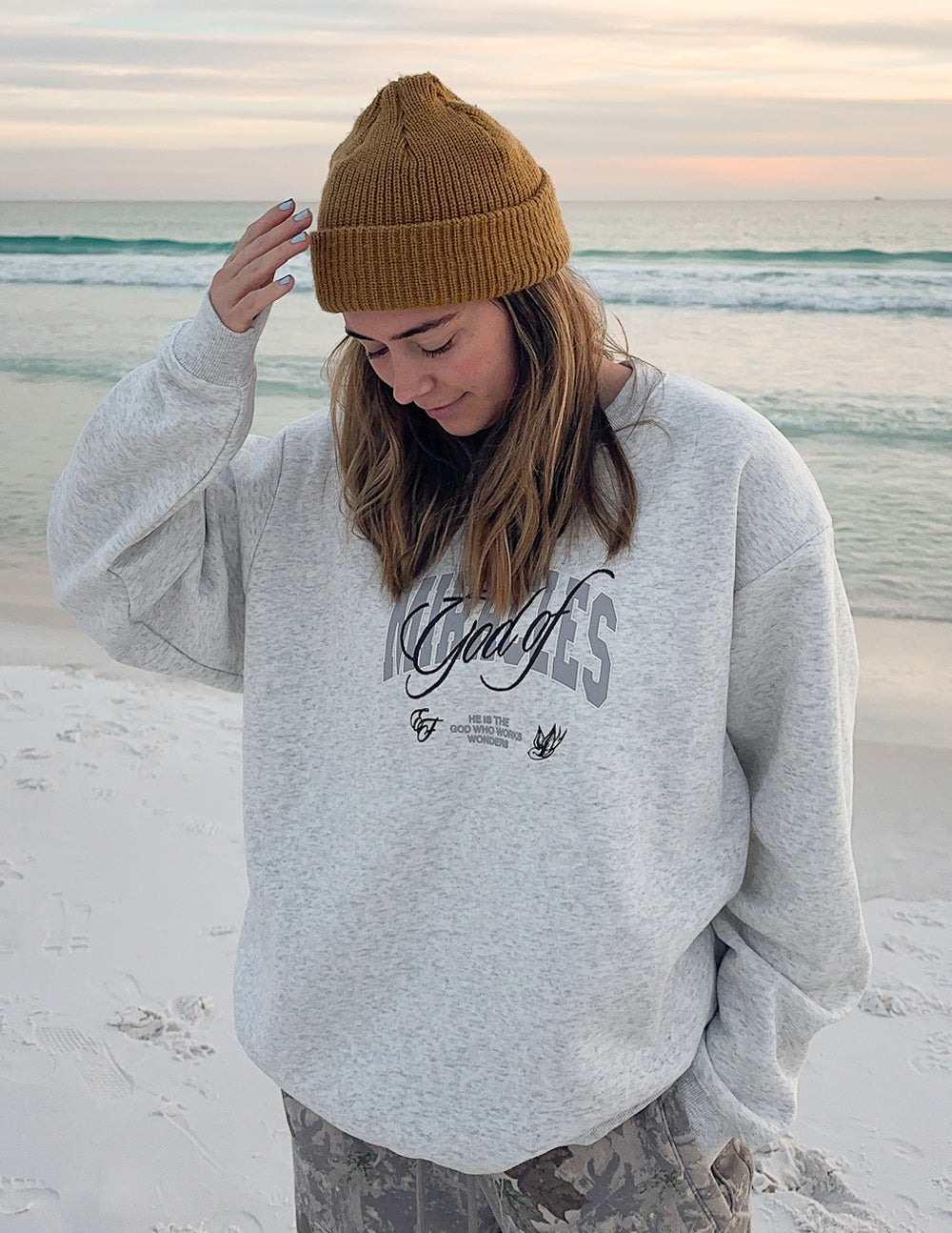 Elevated Faith Christian Crewneck Sweatshirt in light gray worn by a woman on the beach at sunset