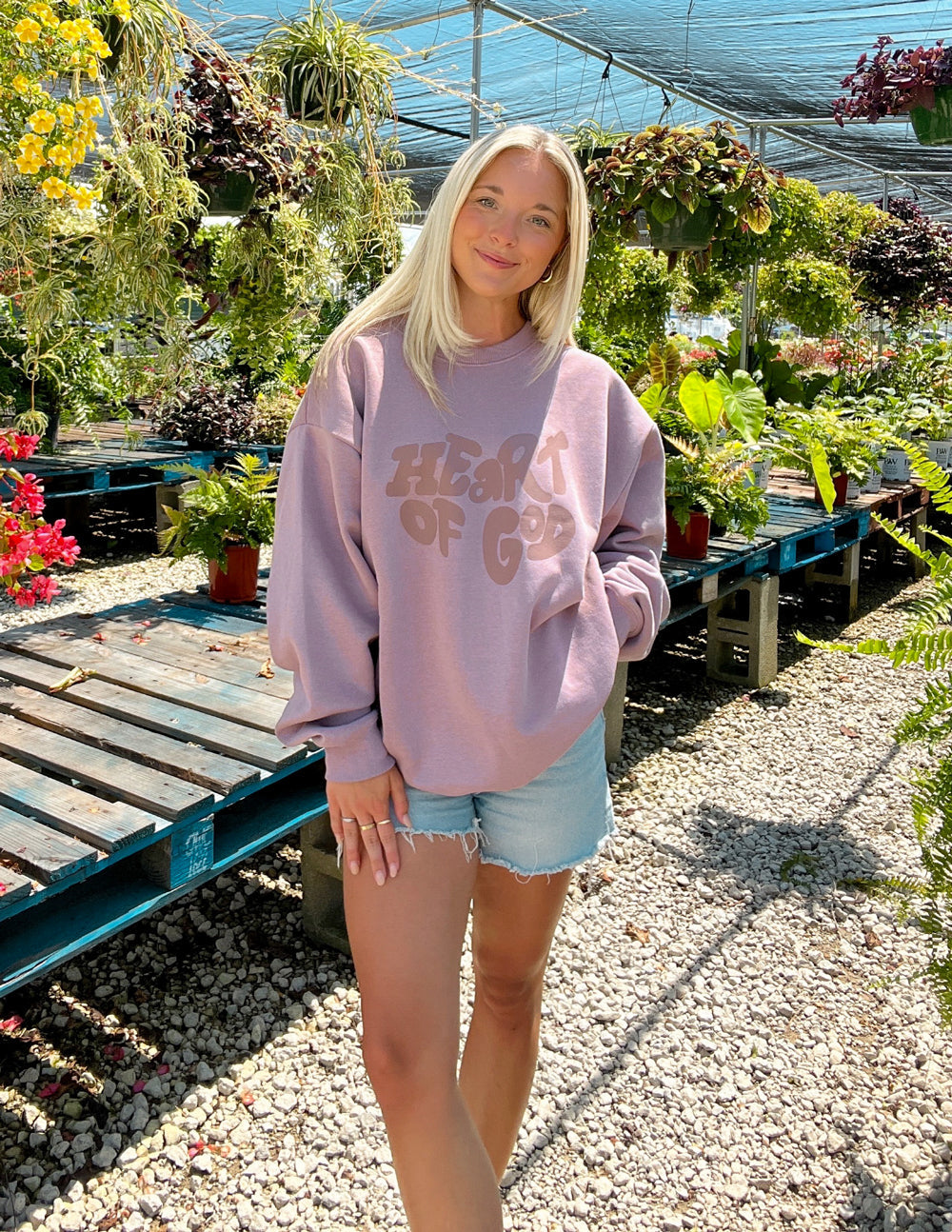 Woman wearing a Heart of God Christian Crewneck Sweatshirt in a garden setting