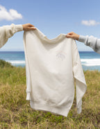 Elevated Faith Christian Crewneck Sweatshirt in cream color displayed against a scenic beach background