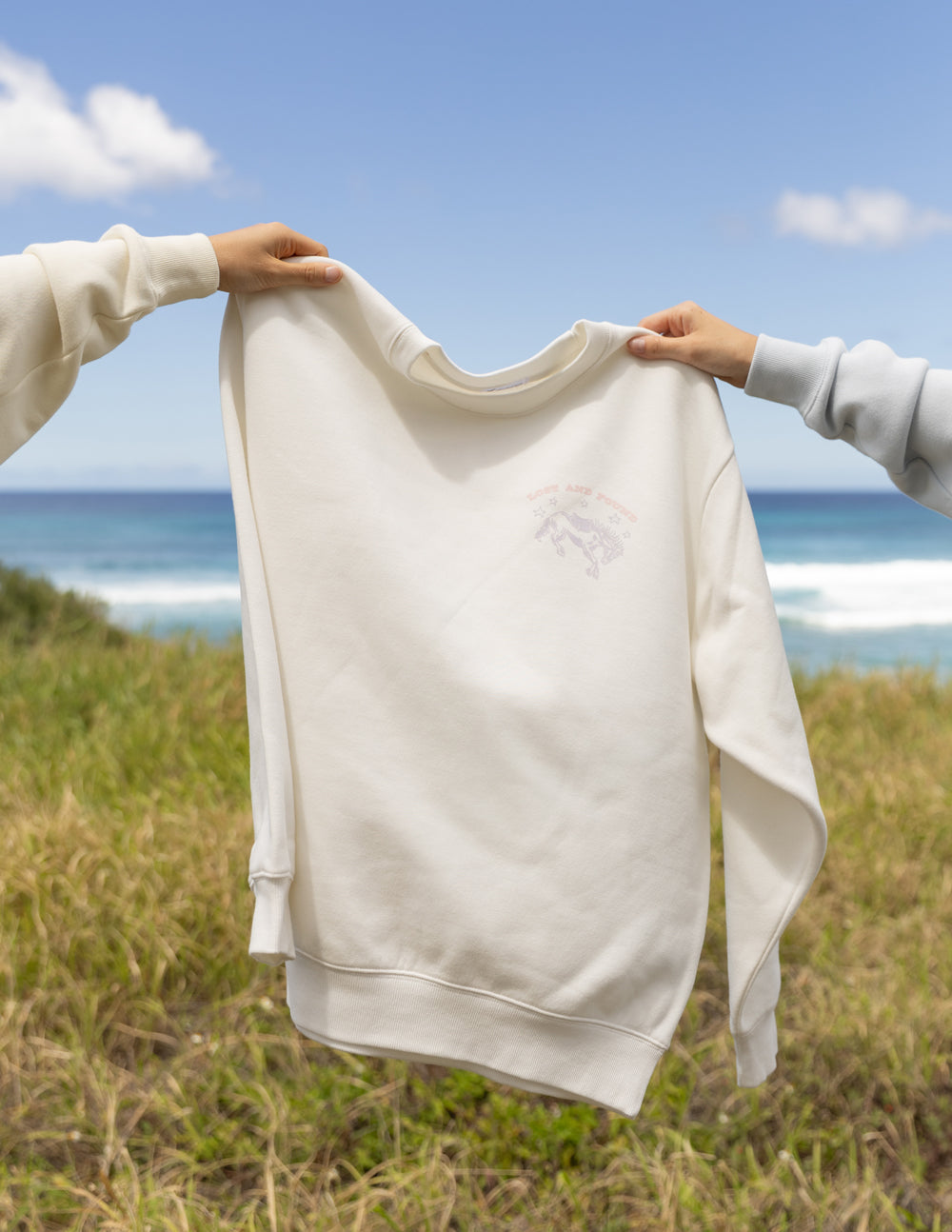 Elevated Faith Christian Crewneck Sweatshirt in cream color displayed against a scenic beach background