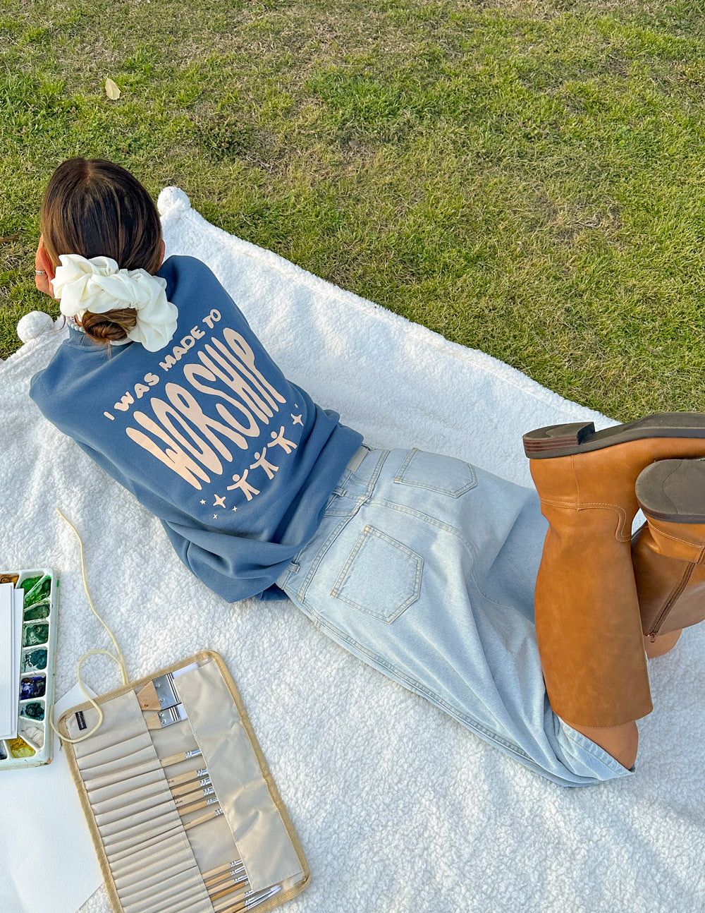 Woman lounging on a blanket in a blue Christian Crewneck Sweatshirt with inspiring text on the back