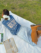 Woman lounging on a blanket in a blue Christian Crewneck Sweatshirt with inspiring text on the back