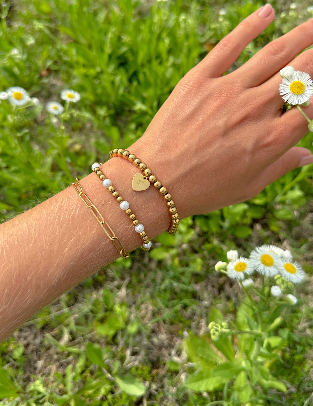 Elevated Faith Christian Jewelry Bracelet set featuring gold and pearl beads on a hand surrounded by flowers
