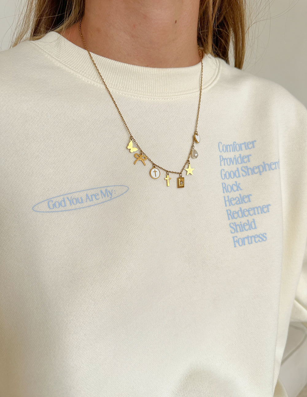 Elevated Faith Christian Jewelry Necklace with Charms and Symbols on a Person Wearing a Cream Sweatshirt