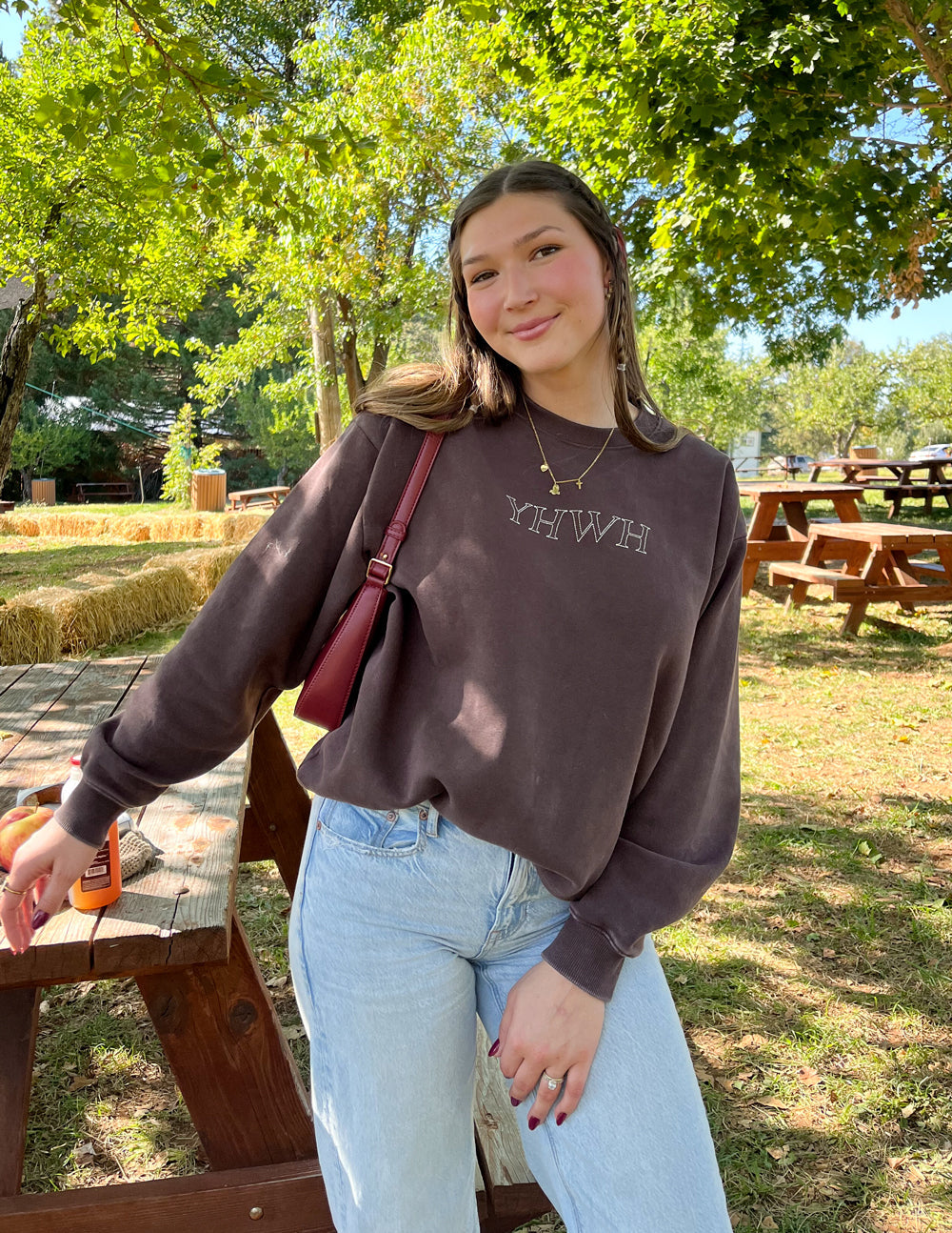 Casual woman wearing a Christian Crewneck Sweatshirt in brown with YHWH lettering outdoors