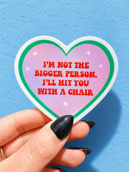 Funny Heart-shaped sticker with pink design, green border, red quote text, held in fingers
