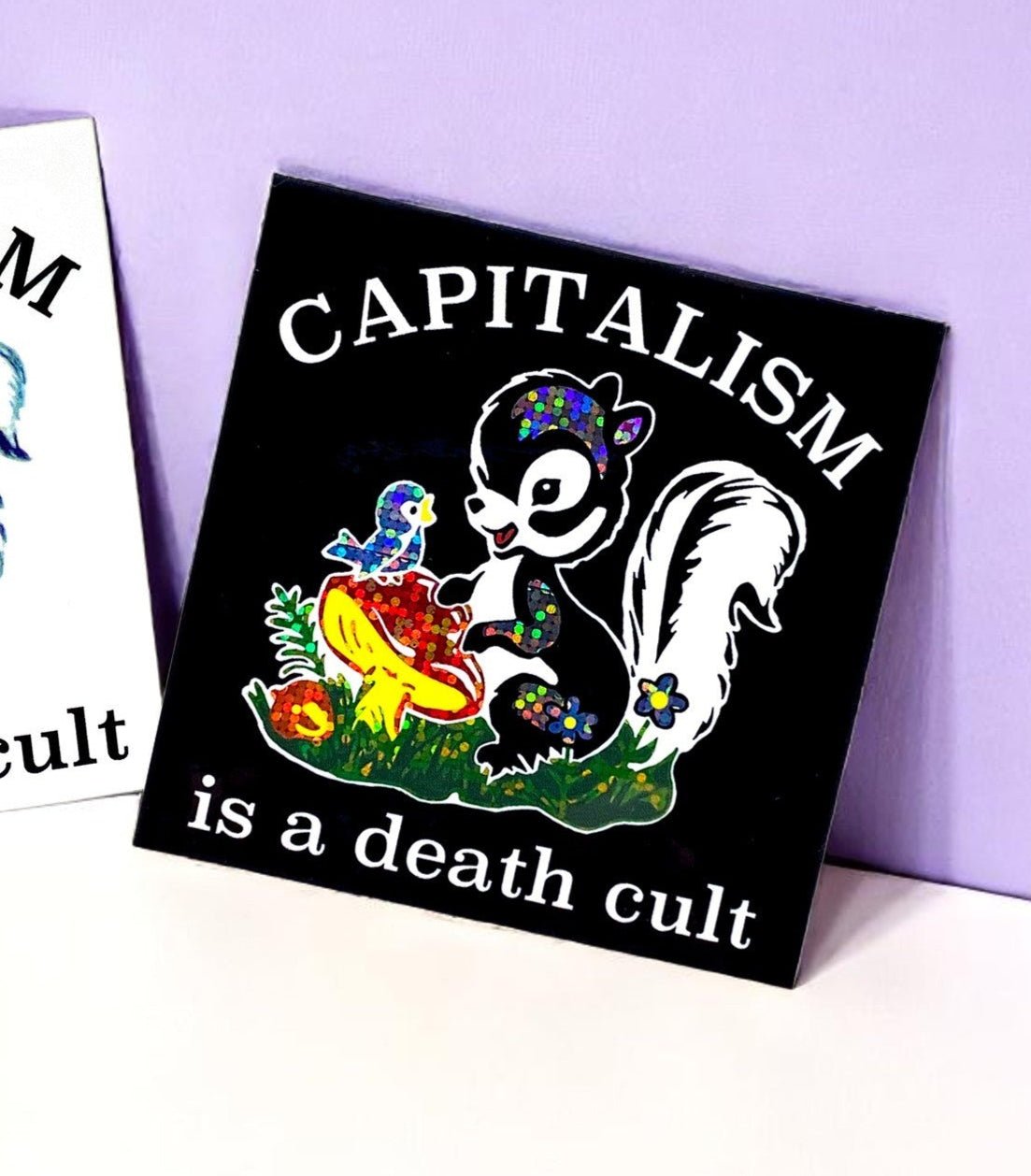Funny Black square sticker with CAPITALISM and “is a death cult” text, skunk illustration.