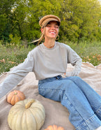Woman wearing a light gray Christian Apparel T-Shirt outdoors, sitting on a blanket with pumpkins