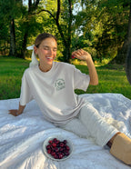 Elevated Faith Christian Apparel T-Shirt in light color, worn by a smiling woman outdoors, sitting on a blanket