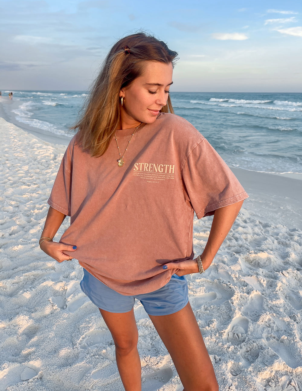 Elevated Faith Christian Apparel T-Shirt in Pink with 'STRENGTH' Graphic on the Beach