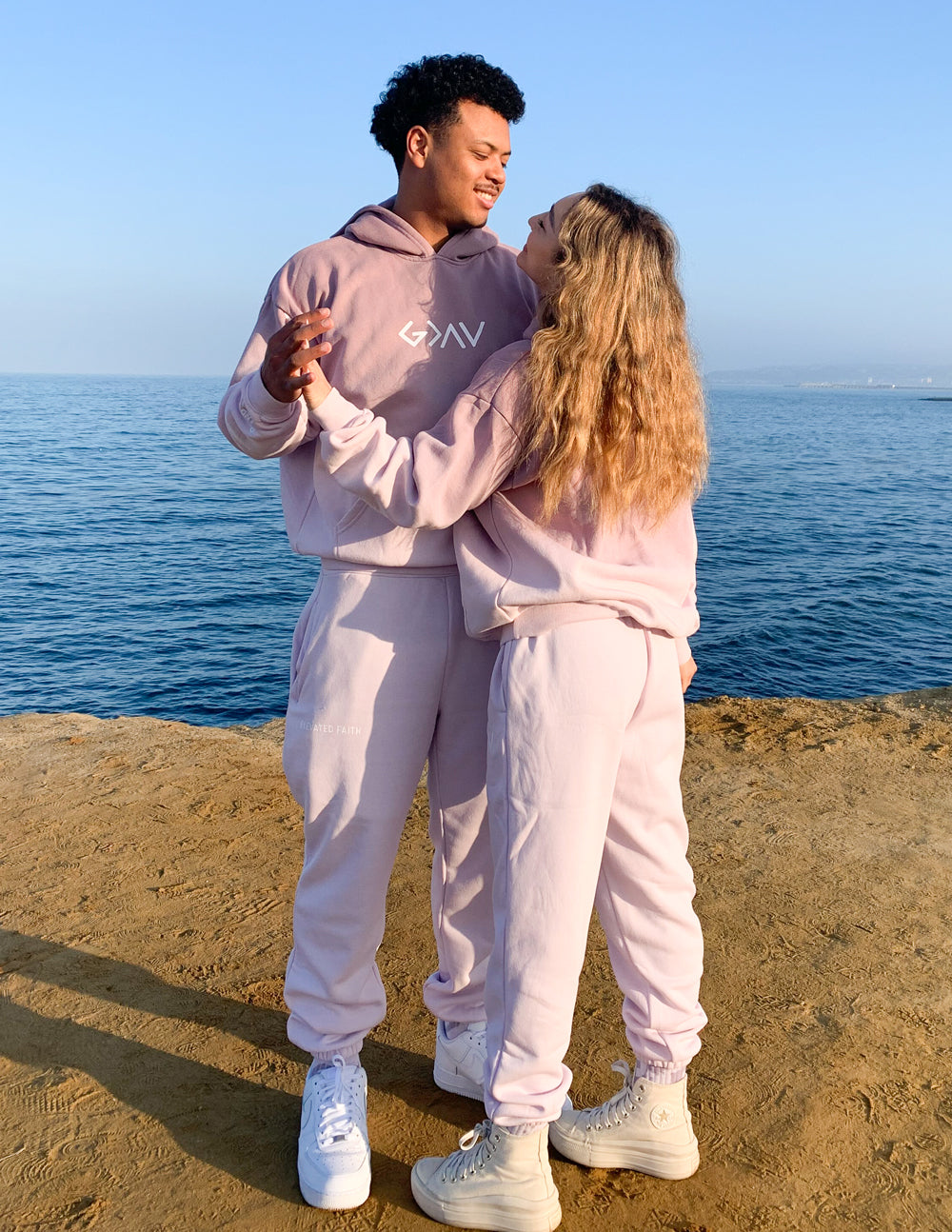 Couple wearing Elevated Faith Christian Hoodie in soft pink near the water for a stylish look