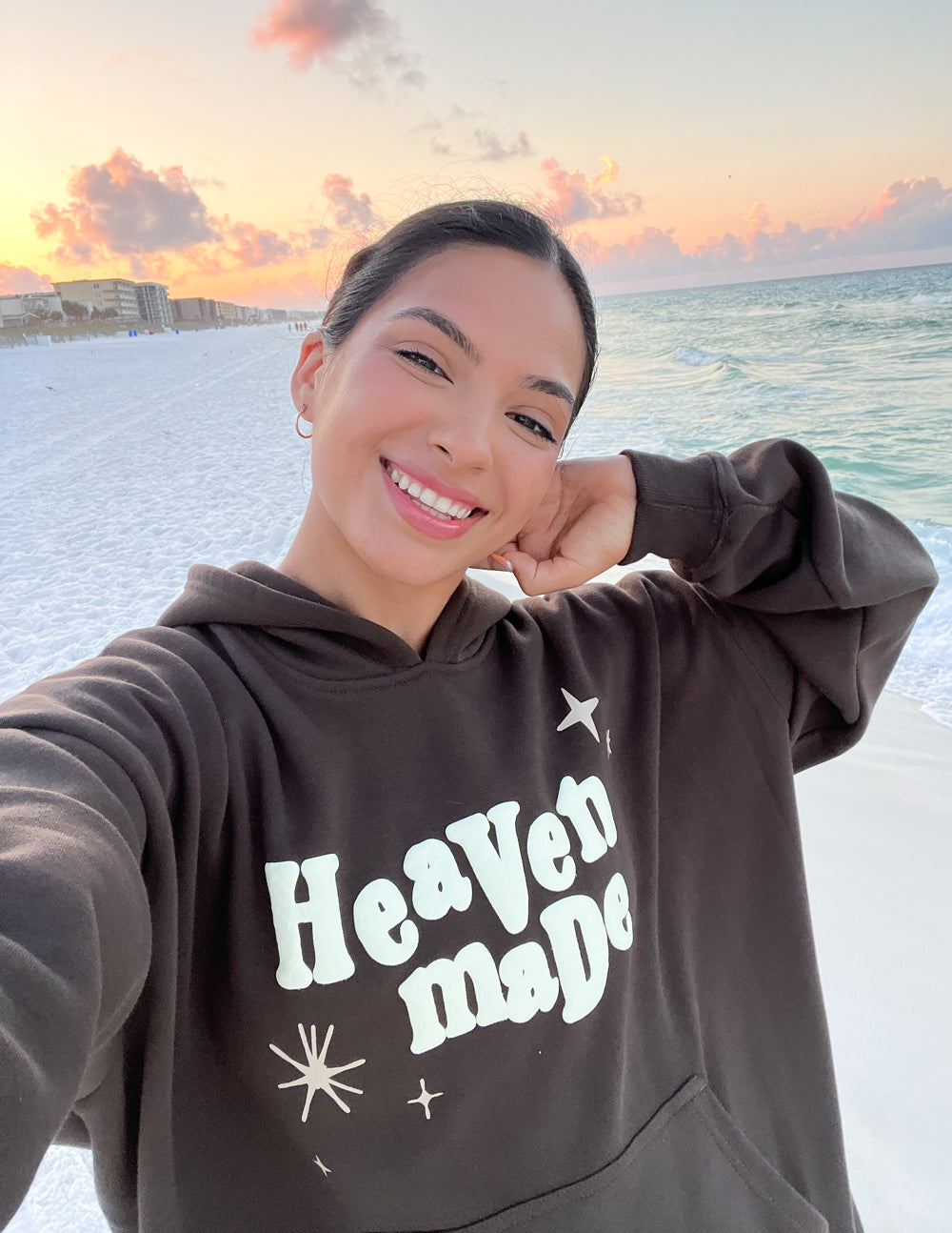 Woman wearing a brown Christian Hoodie with 'Heaven Made' design on a beach at sunset