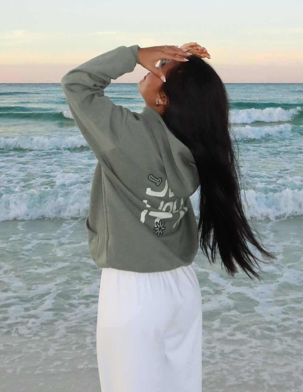 Woman wearing an Elevated Faith Christian Hoodie at the beach with ocean waves in the background