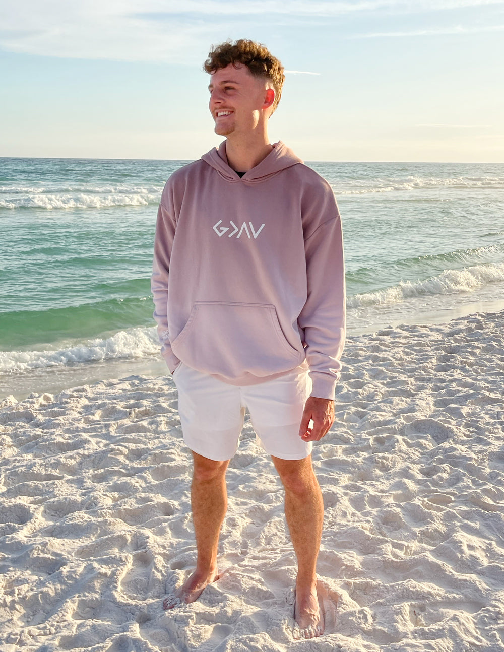 Elevated Faith Christian Hoodie in Light Pink Worn by a Man on the Beach During Sunset
