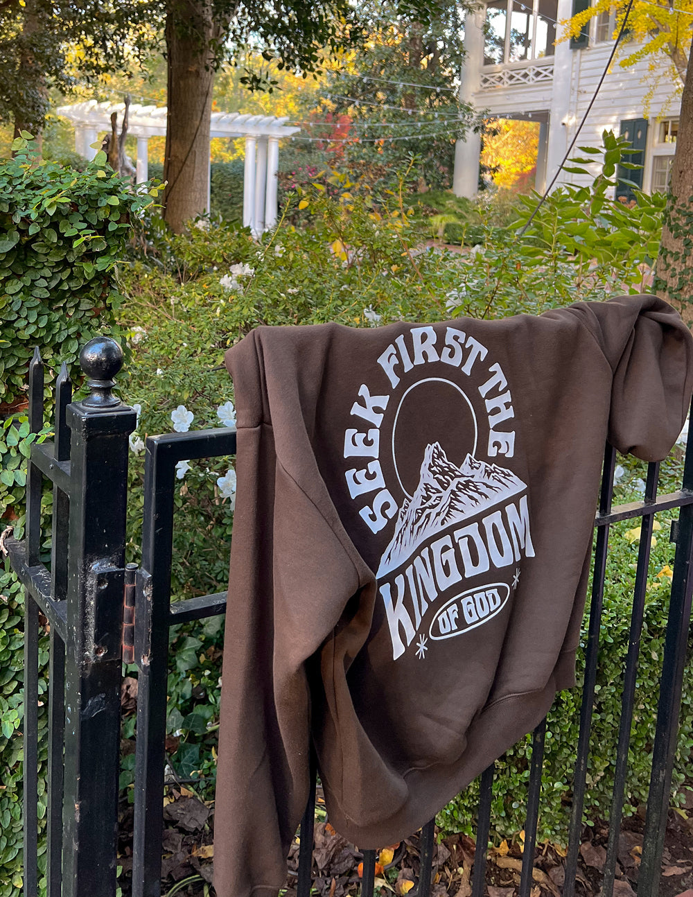Brown Christian Hoodie with 'Seek First the Kingdom of God' Graphic Design on a Fence