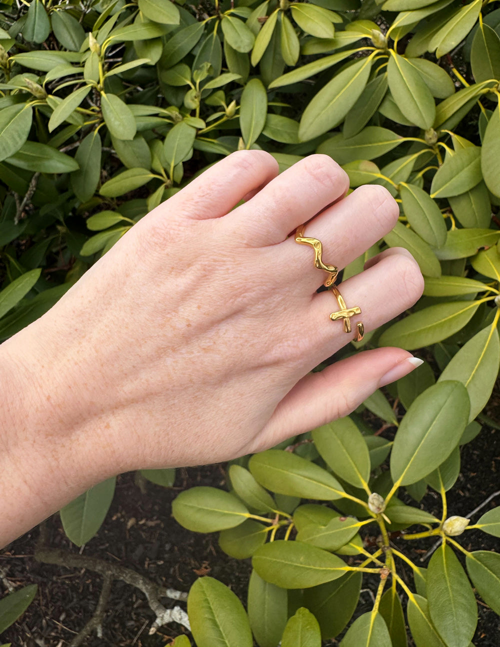 Gold Christian Jewelry rings featuring a cross design, worn on fingers among green leaves