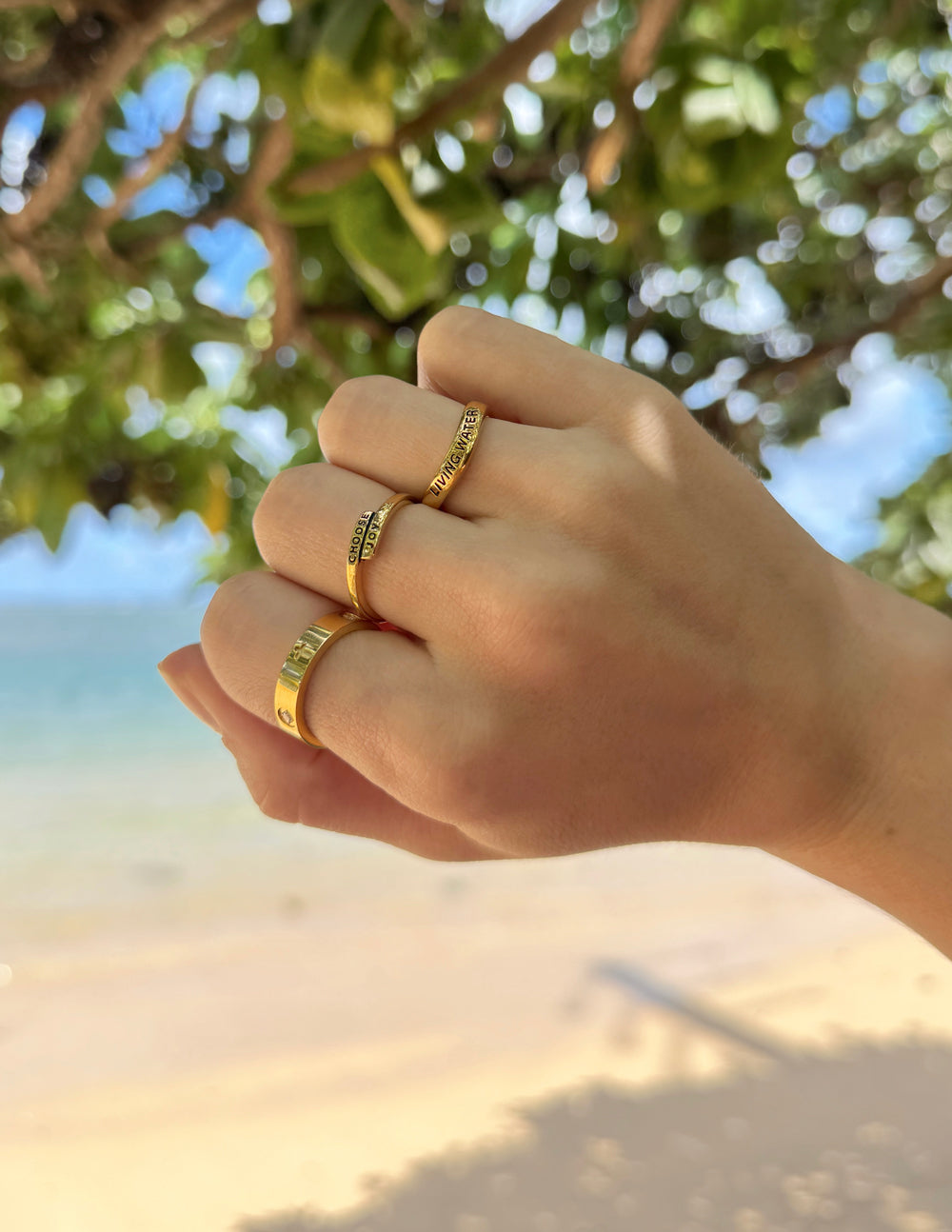 Elevated Faith Christian Jewelry Gold Rings shown on a hand against a beach background
