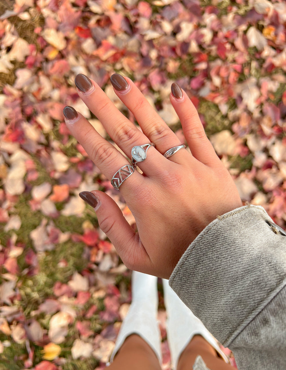 Hand adorned with Elevated Faith Christian Jewelry rings on a bed of colorful autumn leaves