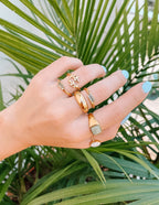 Elevated Faith Christian Jewelry featuring stylish gold rings displayed on a hand among tropical leaves