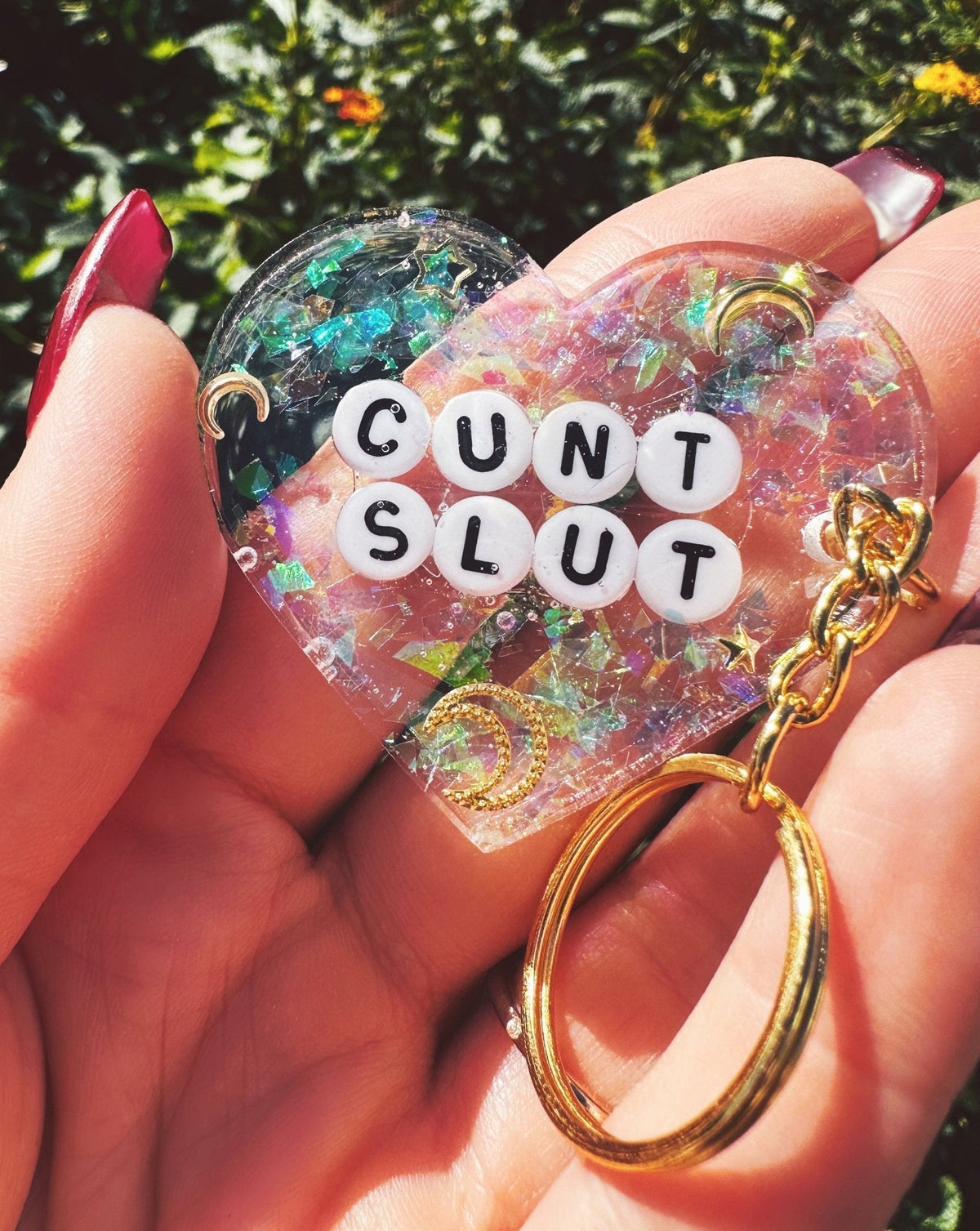 Funny Glitter heart keychain with white 'CUNT SLUT' letters and gold keyring, held in hand
