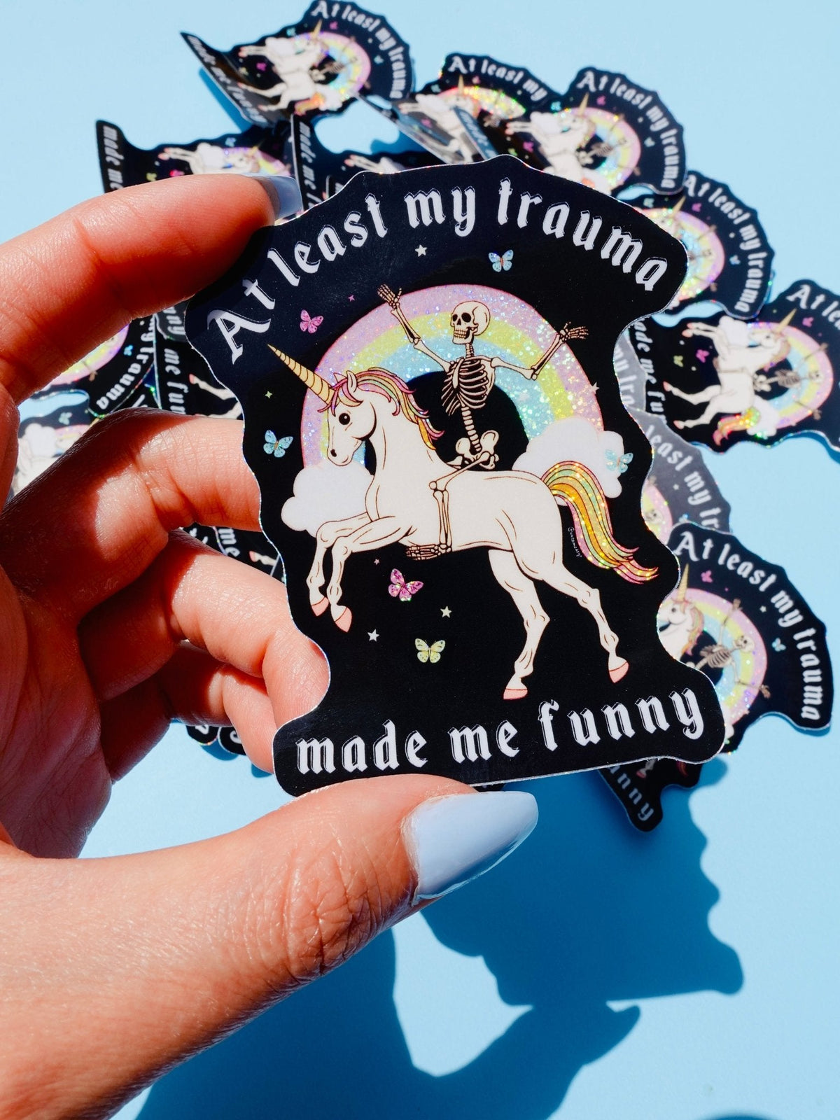 Funny Black unicorn sticker with rainbow halo and skeleton, held in hand