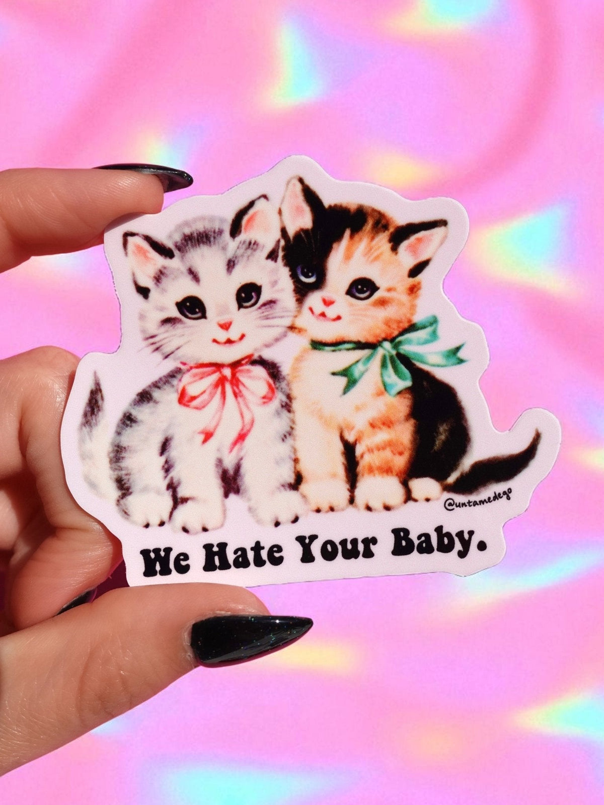 Funny Cat and kitten sticker with "We Hate Your Baby." text, held up by fingers