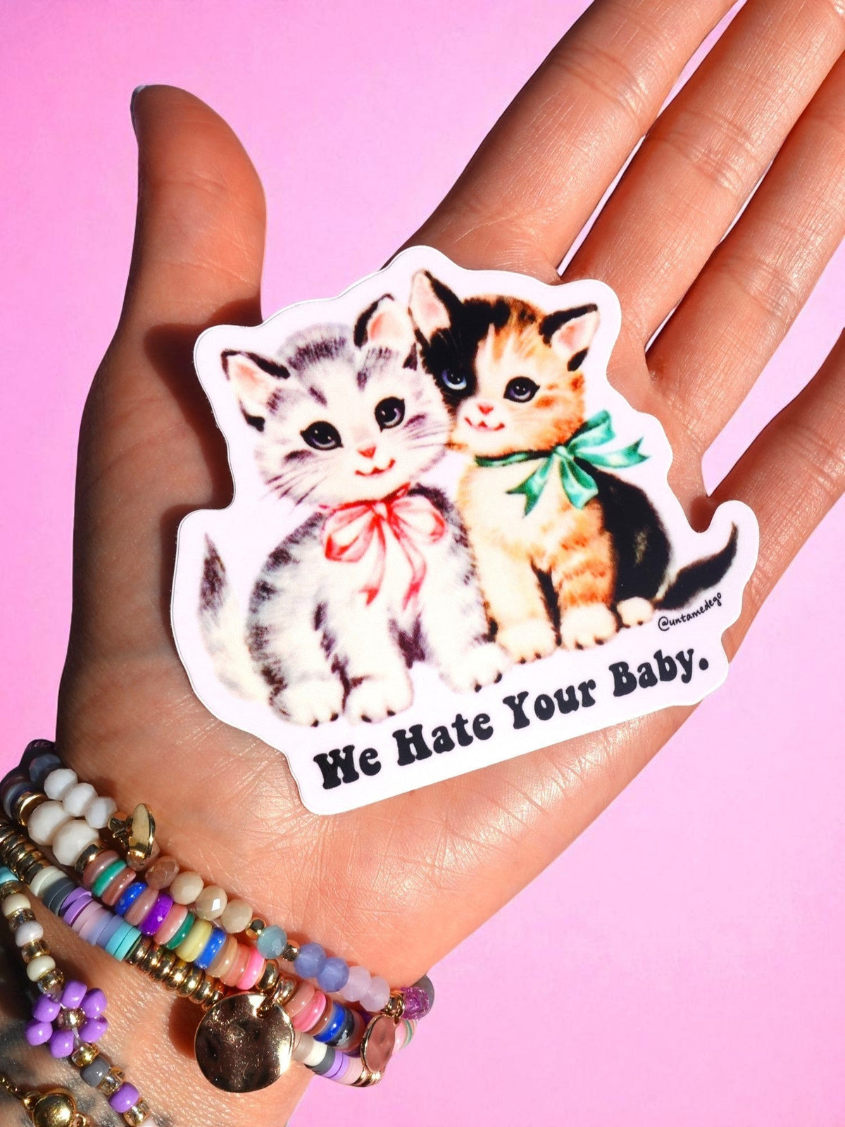 Funny Cat and kitten sticker with "We Hate Your Baby." text on open palm with bracelets