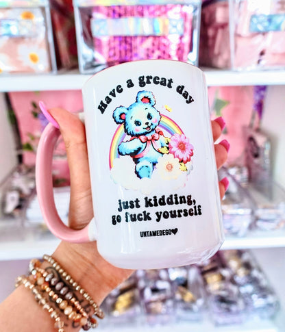 Funny "Have A Great Day Just Kidding" — White mug with pink handle and bear illustration with humorous text, in hand
