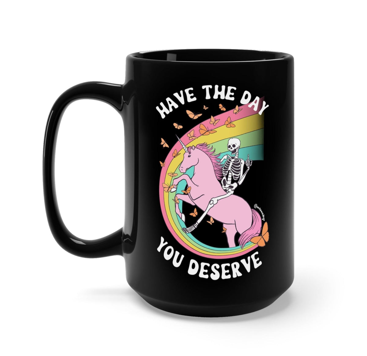 Funny "Have The Day You Deserve" — Black ceramic mug with colorful unicorn and skeleton graphic, slogan text