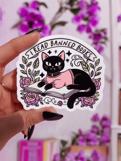 Funny Hand holding cat reading open book sticker with roses, leaves, and 'I Read Banned Books'