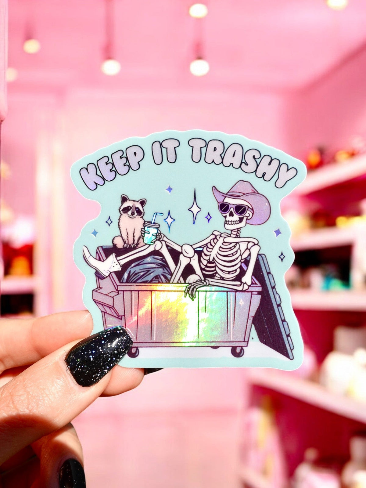 Funny Keep It Trashy sticker with cat and skeleton in trash can, rainbow holographic border