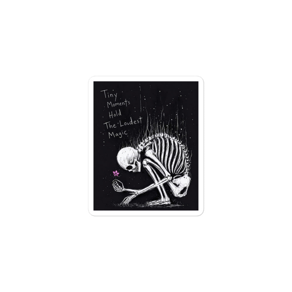 3 x 3 inch 'Tiny Moments' goth sticker featuring a kneeling skeleton holding a tiny pink flower on a black background, with the words "Tiny moments hold the loudest magic"