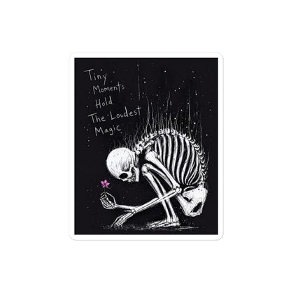 4 x 4 inch 'Tiny Moments' goth sticker featuring a kneeling skeleton holding a tiny pink flower on a black background, with the words "Tiny moments hold the loudest magic"