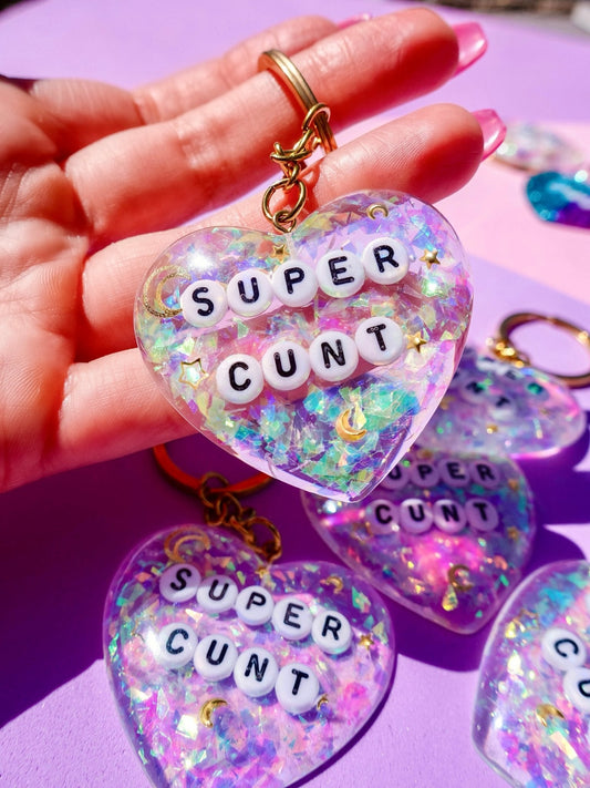 Funny Heart-shaped glitter keychains with gold rings and letter beads spelling SUPER and CUNT