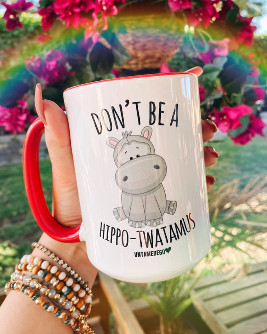 Funny "Don't Be A Hippotwatamus" — White ceramic mug with red handle, hippo graphic and slogan text, held in hand