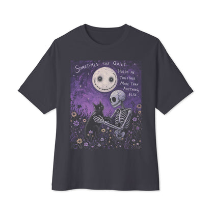 Dark grey oversized boxy tee with the 'The Quiet Heals' goth graphic: a skeleton and a black cat in a purple flower field under a smiling moon, with the words "Sometimes the quiet holds me together more than anything else"
