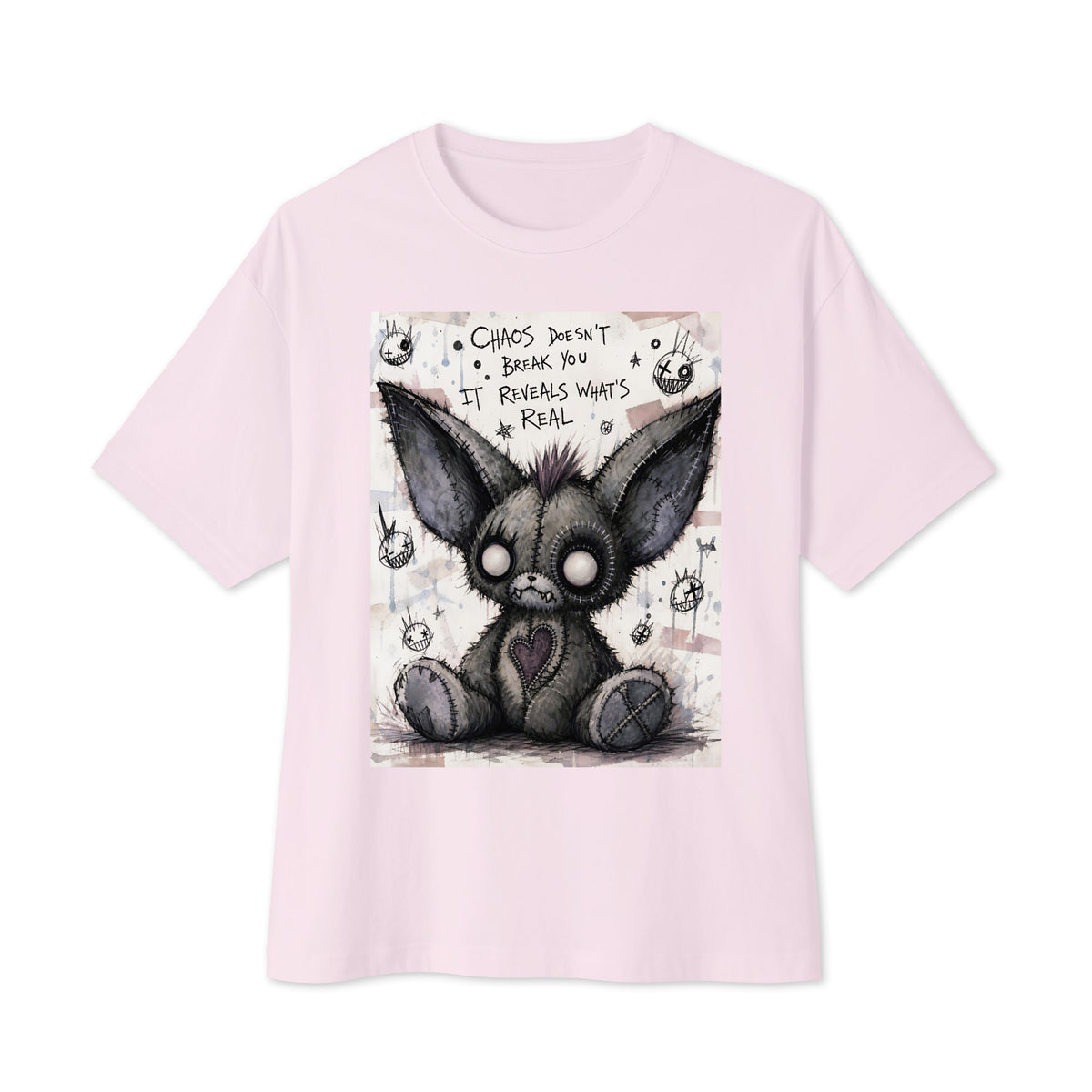 Soft pink oversized boxy tee with the 'Chaos' goth graphic: a stitched gray big-eared creature with button eyes, with the words "Chaos doesn't break you, it reveals what's real"