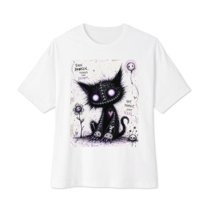 White oversized boxy tee with the 'Even Broken Things Can Bloom' goth graphic: a stitched black cat with glowing purple eyes beside a flower, with the words "Even broken things can bloom"