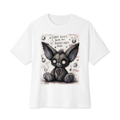 White oversized boxy tee with the 'Chaos' goth graphic: a stitched gray big-eared creature with button eyes, with the words "Chaos doesn't break you, it reveals what's real"