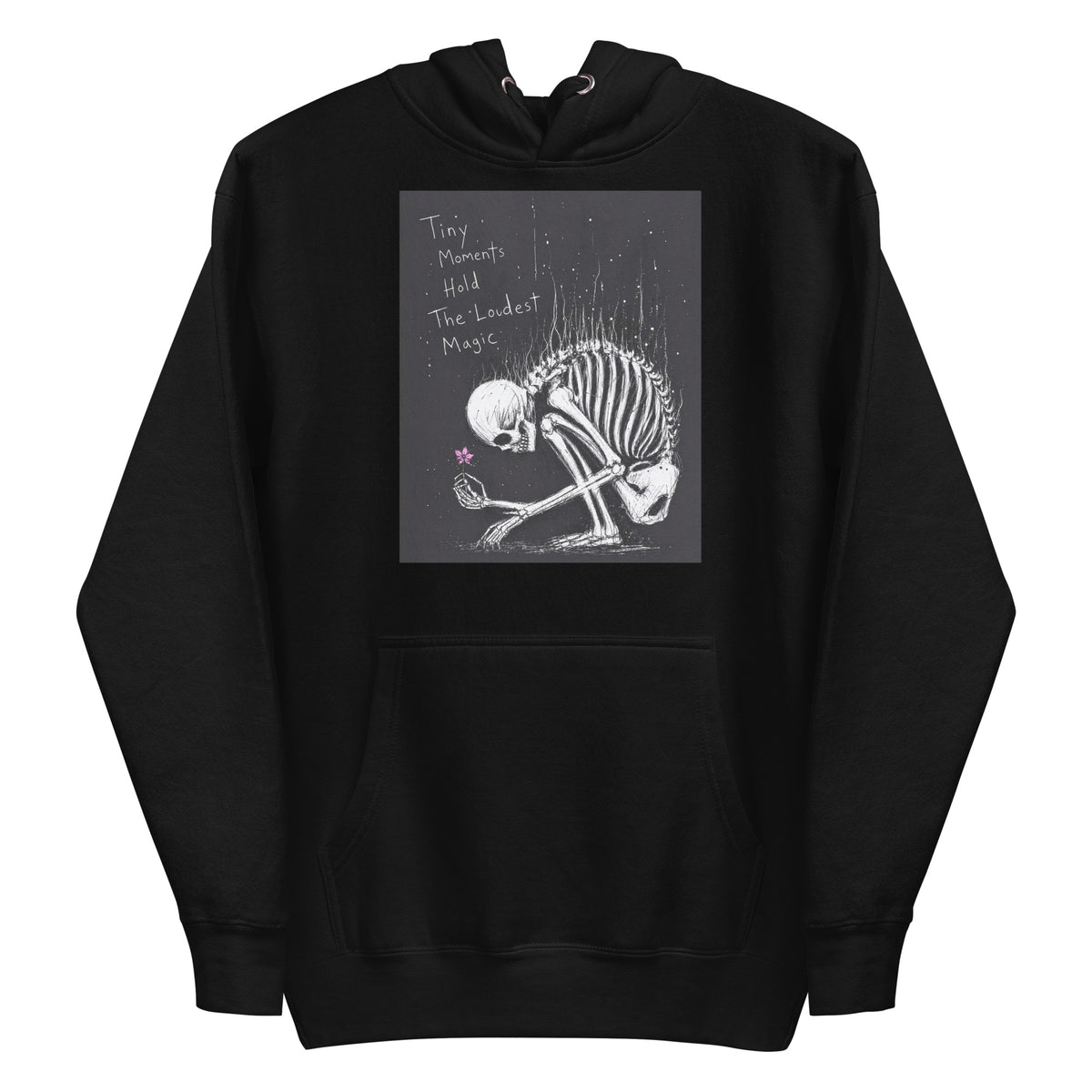 Black pullover hoodie with the 'Tiny Moments' goth graphic: a kneeling skeleton holding a tiny pink flower on a black background, with the words "Tiny moments hold the loudest magic"