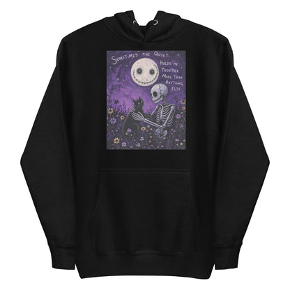 Black pullover hoodie with the 'The Quiet Heals' goth graphic: a skeleton and a black cat in a purple flower field under a smiling moon, with the words "Sometimes the quiet holds me together more than anything else"