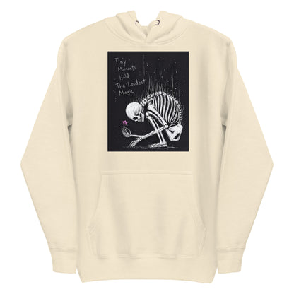 Bone pullover hoodie with the 'Tiny Moments' goth graphic: a kneeling skeleton holding a tiny pink flower on a black background, with the words "Tiny moments hold the loudest magic"